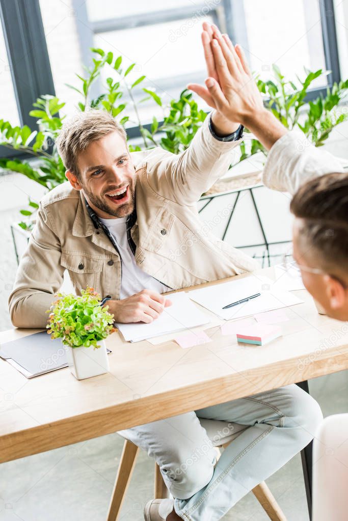 young, handsome businessmen giving high five while sitting at workplace in office
