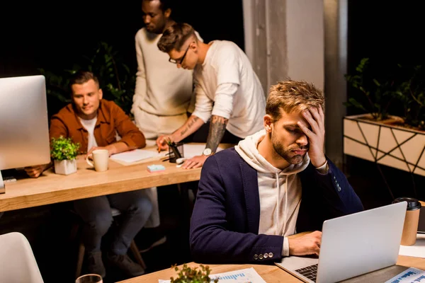 Empresário Exausto Usando Laptop Enquanto Trabalhava Escritório Noite Perto Colegas — Fotografia de Stock