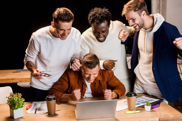 Jóvenes Empresarios Alegres Pie Cerca Computadora Portátil Mostrando Gesto Ganador — Foto de Stock