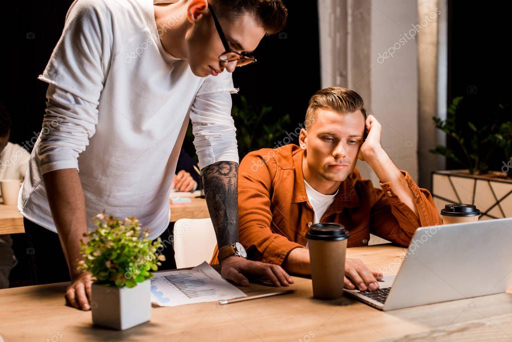 joven hombre de negocios de pie cerca de colega agotado utilizando el