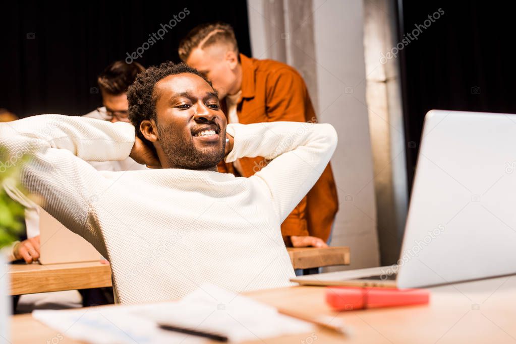 happy african american businessman looking at laptop while working at night with colleagues