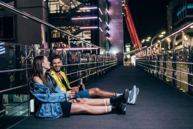 gece şehirde oturan şişe ve gülümseyen kız arkadaşı ile erkek arkadaşı yan görünümü 
