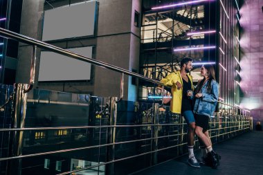 yakışıklı erkek arkadaşı ve çekici kız arkadaşı yan görünümü gülümseyerek ve gece şehirde konuşurken 