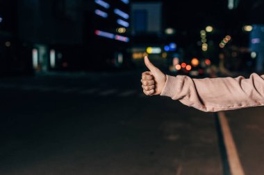 gece şehirde başparmak gösteren genç kadının kırpılmış görünümü 