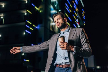 resmi giyim yakışıklı işadamı otostop ve gece şehirde kağıt bardak tutarak 
