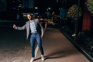 resmi giyim yakışıklı işadamı başparmak ve gece şehirde gülümseyen 