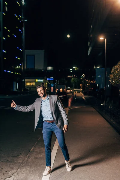 Przystojny Biznesmen Posiadanie Nosić Uśmiechnięty Thumbing Noc Miasto — Zdjęcie stockowe