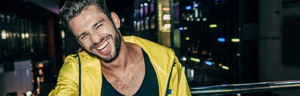 stock image panoramic shot of handsome man in yellow jacket smiling in night city 