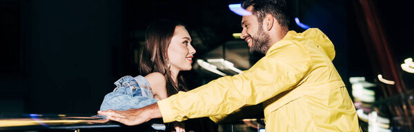 panoramic shot of smiling boyfriend and girlfriend looking at each other in night city 