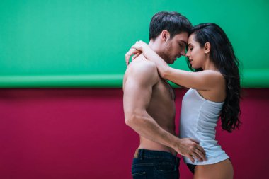 Kolsuz tişörtsüz ve külotlu seksi kız kırmızı ve yeşil arka planda üstsüz erkek arkadaşı kucaklıyor.