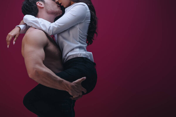 cropped view of shirtless man holding on hands and kissing girl in white shirt on dark background
