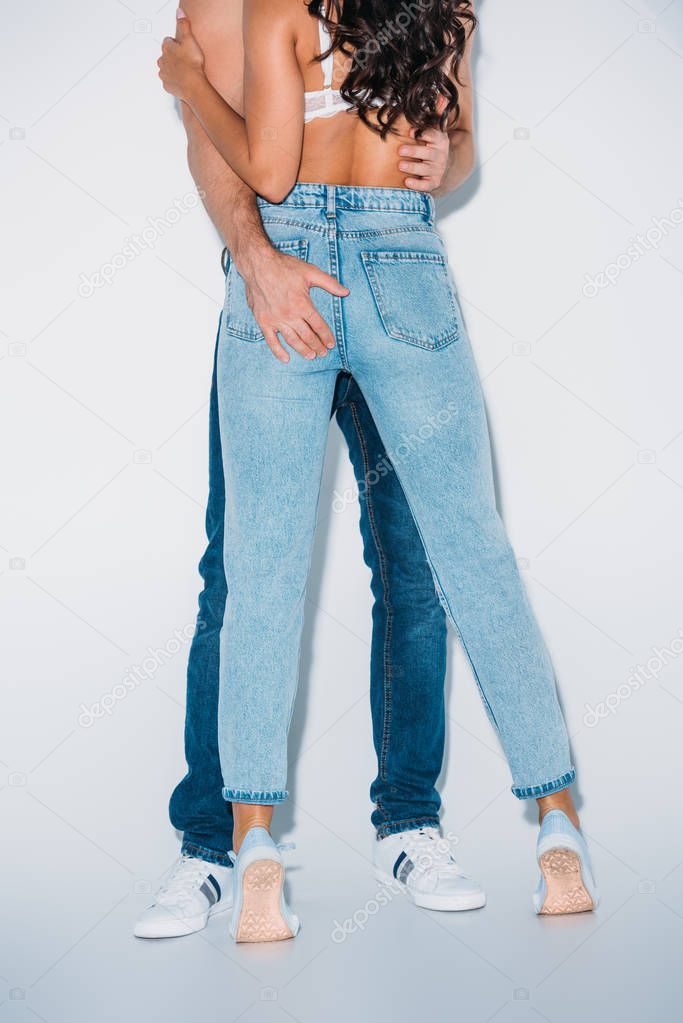 partial view of man touching buttocks of girl in blue jeans on grey background