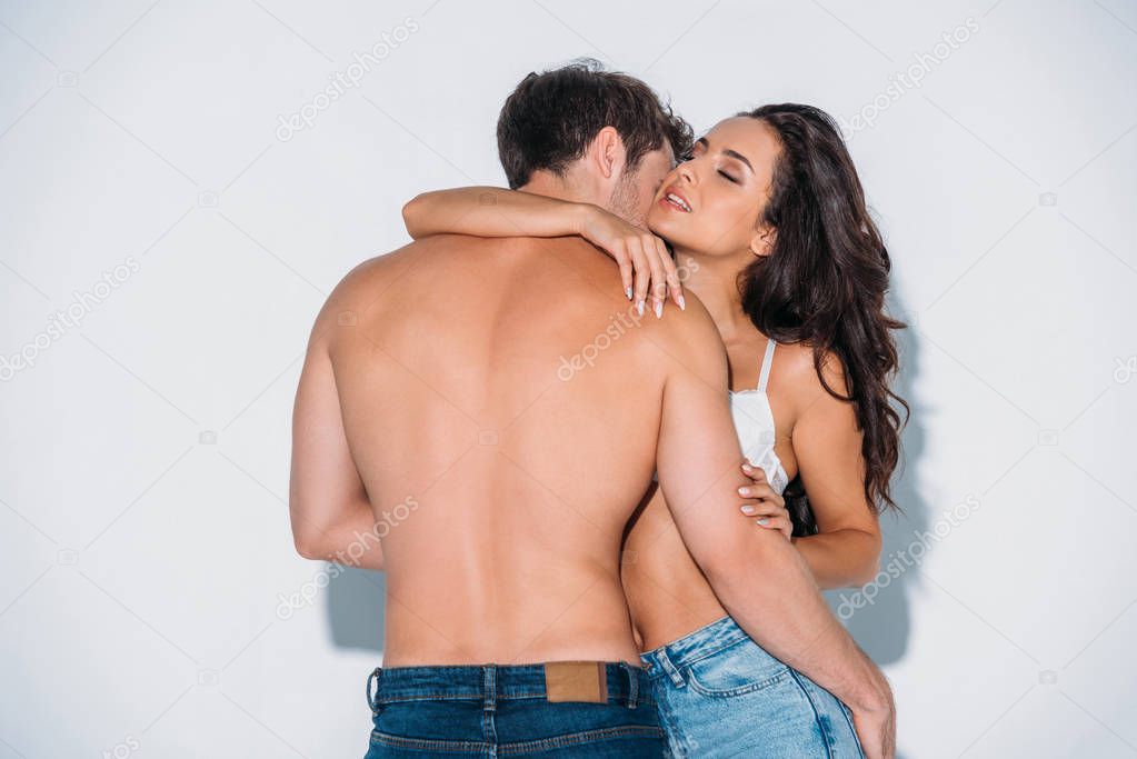 back view of shirtless young man embracing sexy girl in white bra on grey background