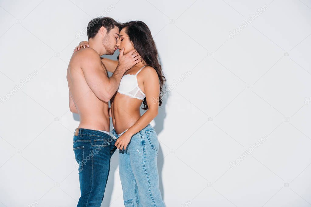 young man kissing girl unbuttoning his jeans on grey background