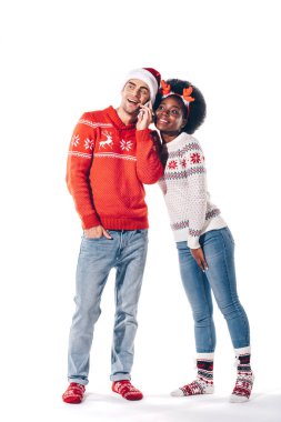 Noel Baba şapkası ve geyik boynuzları takan çok kültürlü bir çift akıllı telefondan konuşuyor.