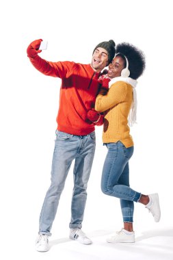 Irklar arası güzel bir çift akıllı telefondan selfie çekiyor, beyaz telefondan izole edilmiş.