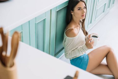 Kahveli çekici genç bir kadın mutfakta yerde oturuyor.