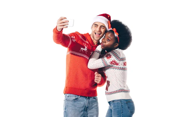 戴着桑塔帽 头戴鹿角 拿着智能手机自私自利 与白人隔离的快乐的跨种族夫妇 — 图库照片