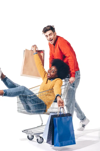 Çok Irklı Mutlu Bir Çift Alışveriş Arabasında Alışveriş Torbalarıyla Eğleniyor — Stok fotoğraf