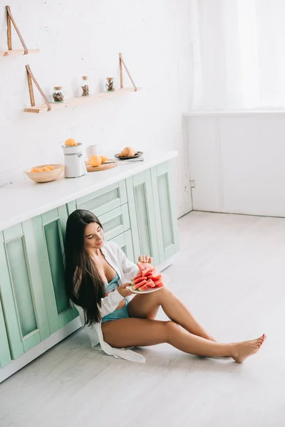 穿着内衣和白衬衫的快乐女人在厨房的地板上吃西瓜 — 图库照片