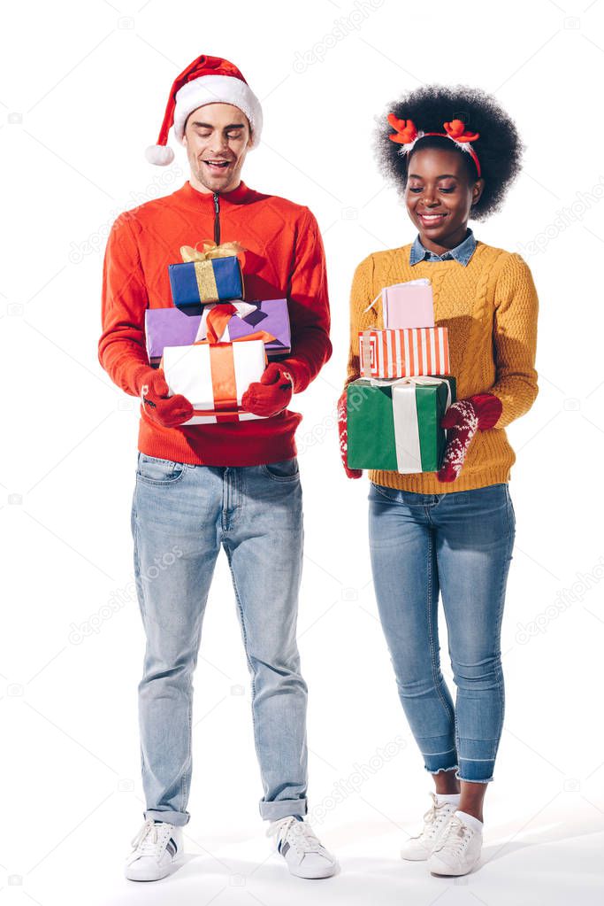 multiethnic couple in santa hat and deer horns holding christmas gifts, isolated on white