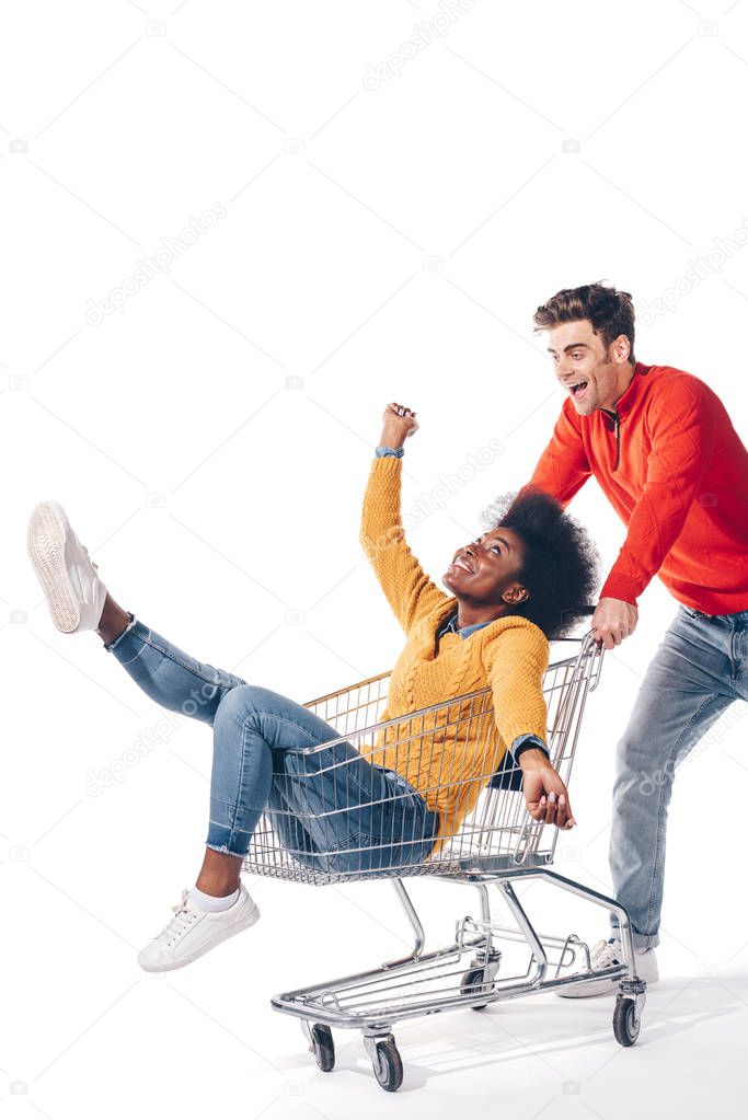 beautiful interracial couple having fun with shopping cart, isolated on white