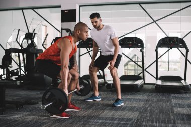 Afrika kökenli Amerikan sporcusuna bakan konsantre antrenör halter kaldırıyor.