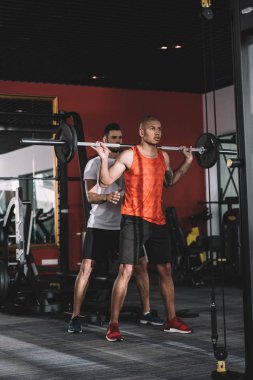 Afrika kökenli Amerikalı sporcuyu kontrol eden eğitimci halteri kaldırıyor.