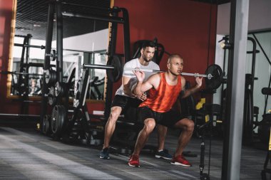 Genç Afro-Amerikan sporcusunu destekleyen özenli antrenör halter kaldırıyor.