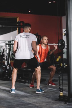 Genç Afro-Amerikan sporcusunu destekleyen kişisel antrenör halter kaldırıyor.