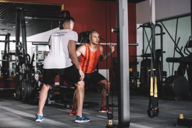 Genç Afro-Amerikan sporcunun halter kaldırmasını denetleyen kişisel eğitmenin arka görünüşü