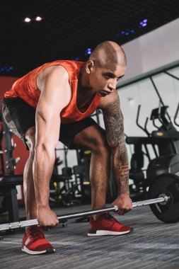 Genç, konsantre olmuş Afrikalı Amerikan sporcusu spor salonunda halter kaldırıyor.