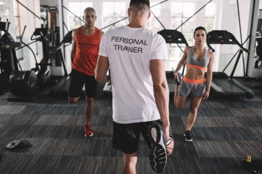 Spor salonunda ısınan çok kültürlü sporcuları denetleyen kişisel antrenörlerin arka planı