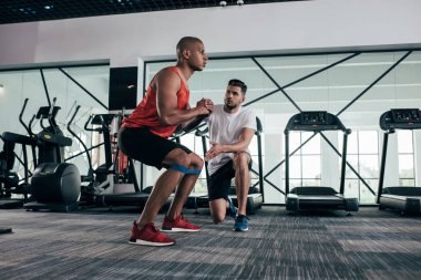 Spor salonunda ısınan Afrikalı Amerikalı genç sporcuya dikkatle bakan antrenör.
