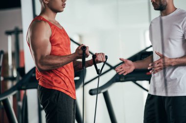 Afrika kökenli bir Amerikan sporcusunun yanında duran ve daha geniş bir alanda spor yapan antrenör görüşü.