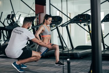 Kişisel antrenör, direniş bandıyla egzersiz yapan genç sporcu kadını eğitiyor.