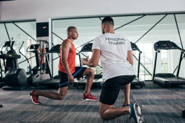 Afrika kökenli Amerikan sporcusuna direniş bandıyla egzersiz yaptıran kişisel antrenörün arka planı.