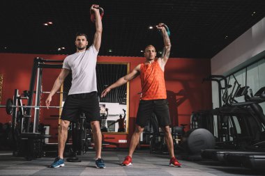 Yakışıklı antrenör, Afrika kökenli Amerikan atletiyle birlikte ağırlık kaldırıyor.
