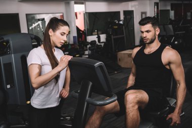 Çekici antrenör yakışıklı sporcuyu eğitiyor ve eliptik eğitici üzerinde çalışıyor. 