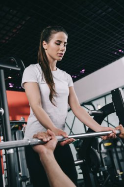 Spor hocasının spor salonunda halteri kaldırmasına yardımcı olan dikkatli antrenör.