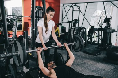 Spor hocasının spor salonunda halteri kaldırmasına yardımcı olan özenli, genç antrenör.