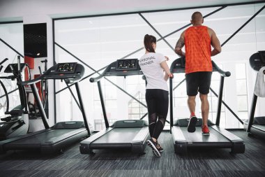 Koşu bandında koşan Afrikalı Amerikalı sporcuyu denetleyen kişisel eğitmenin arka planı