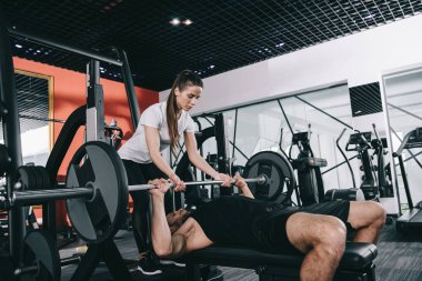 Güzel, özenli antrenör sporcunun spor salonunda halteri kaldırmasına yardım ediyor.