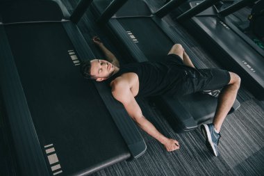 top view of unconscious sportsman lying on treadmill in gym  clipart