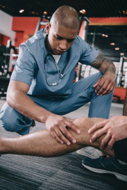 Ciddi bir Afrikalı Amerikalı doktor, sporcunun yaralı dizini inceliyor. 