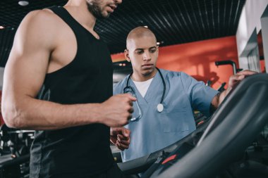 Afrikalı Amerikalı bir doktorun yanında koşu bandındaki sporcu manzarası.