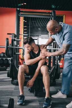 Özenli Afrikalı Amerikalı doktor genç sporcunun yaralı omzuna dokunuyor. 