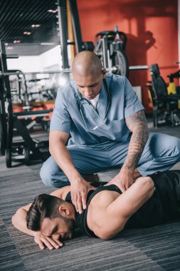 Spor adamının yaralı sırtını muayene eden özenli Amerikalı doktor yerde yatıyor.