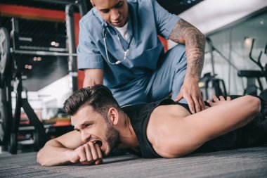 Genç Amerikalı doktor yaralı bir sporcunun sırtına dokunuyor yerde yatıyor ve acıdan kıvranıyor