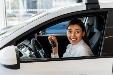 cheerful woman holding car key while sitting in car 